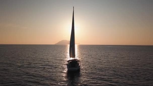 Вид с воздуха на белый парусник, стоящий на якоре в Средиземном море против острова Липари. Солнце отражается на поверхности воды, восход солнца. Сицилия, Италия — стоковое видео