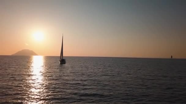 Letecký pohled na bílou plachetnici kotvící ve Středozemním moři proti Lipari Island a skále. Slunce se odráží ve vodě, východ slunce. Sicílie, Itálie — Stock video