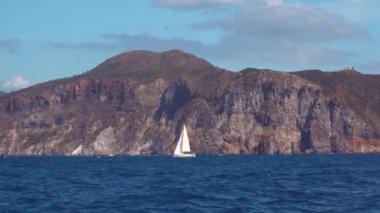 Denizde beyaz yelkenli, mavi gökyüzü ve kayalık dağlar