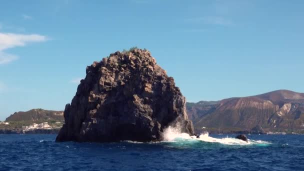 Golven wassen rots in zee tegen bergen, blauwe lucht — Stockvideo