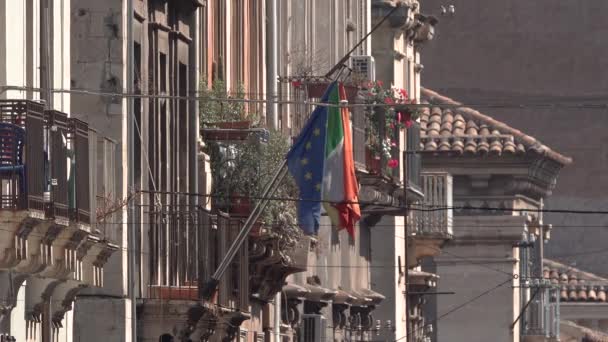 CATANIA, SICILY, ITALY - SEPT, 2019: Old buildings, balconies with flowers in pots and flags of European Union and Italy. Street of historic center — Stock Footage CATANIA, SICILY, ITALY - SEPT, 2019: Old buildings, balconies with flowers in pots and flags of European Union and Italy. Street of historic center Stock Footage