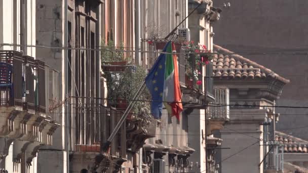 CATANIA, SICILY,イタリア- 2019年9月:古い建物、欧州連合(EU)とイタリアのポットや旗に花のあるバルコニー。歴史的中心部の通り — ストック動画