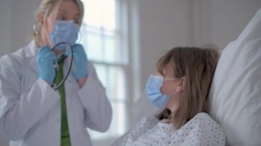 Koruyucu giysiler giyen arkadaş canlısı kadın doktor hastanın kalbini dinler.