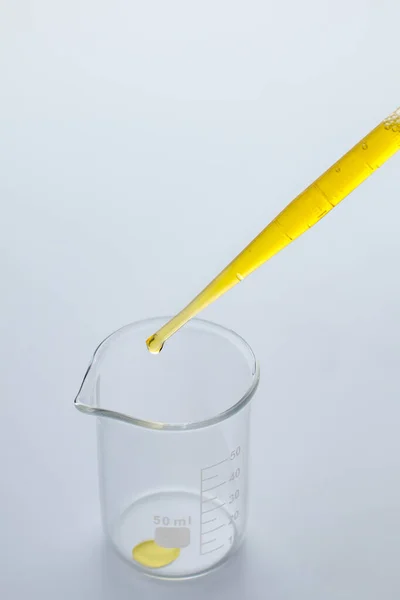 Gele olie uit een plastic pipet in een bekerglas laten vallen — Stockfoto