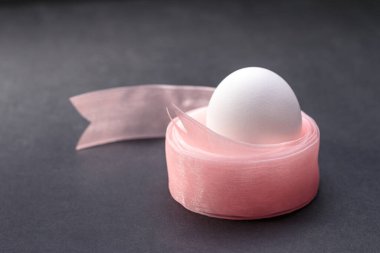 Siyah arka planda Paskalya için pembe dantelle süslenmiş kar beyazı bir yumurta.