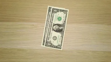Erkek bir sol el, ahşap bir masaya Amerikan dolarlarının farklı banknotlarını koyuyor ve diğer el de nihayet masadaki tüm banknotları alıyor.