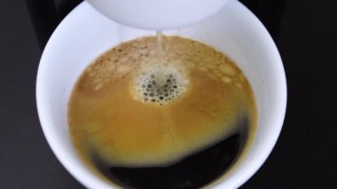 Kahve makinesiyle kahveyi demledikten sonra siyah arka planda beyaz bir fincana, kahve makinesinin son akışını neredeyse dolu bir fincana, yavaş çekimde...