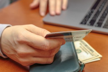 İnternet üzerinden ödeme yaparken kredi kartı tutan, gri dizüstü bilgisayarı ve yeşil çantalı kahverengi bir masada oturan, online alışveriş fikri...