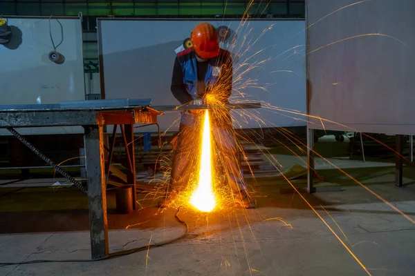 Worker operates angle grinder. Sparks from the angle grinder.