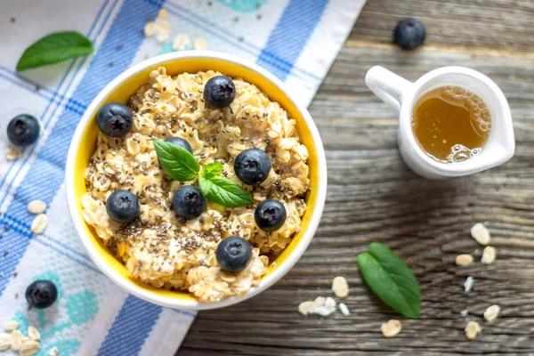 Yulaf lapası - yulaf gevreği yaban mersini ve nane yaprakları mavi ve beyaz masa örtüsü ile ahşap arka plan üzerinde