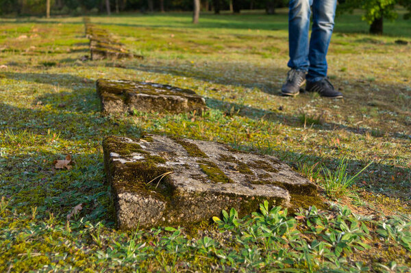 Young man stands near old mossy gravestones in the form of a cross in a war cemetery of soldiers of the First World War