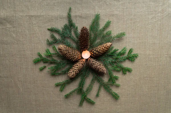 Yeni yıl dekoru: köknar kozalaklarından oluşan bir yıldız, köknar dallarının üzerinde uzanır ve ortasında yanan bir mum bulunur.