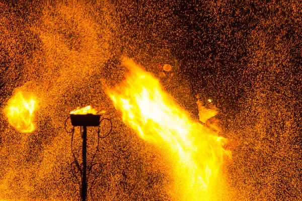 Koruyucu ısıya dayanıklı giysili maskeli adam yangın ve kıvılcımlar saçtığını gösteriyor.