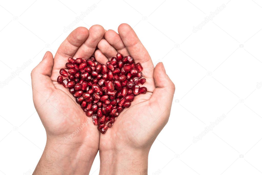 A man holds a heart made of ripe pomegranate seeds in his hands. Care of the heart and love.
