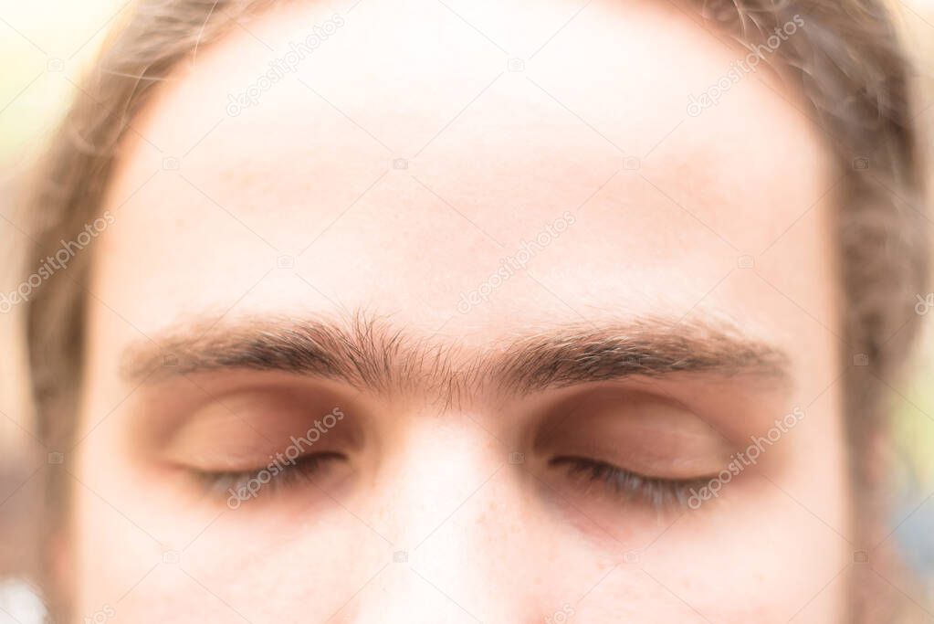 Close up fused eyebrows of a young man of European appearance. The grooming on the face. Men's cosmetology. Soft focus.