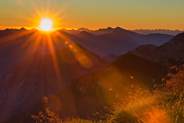 Rood oranje zonsondergang met zonnestralen aan het gras in de bergen van Tirol — Stockfoto