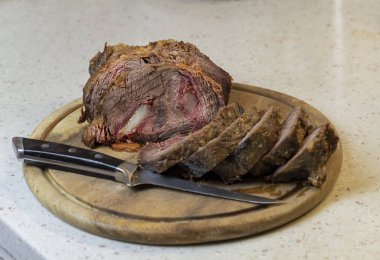 Ahşap kesme tahtasına dilimlenmiş fırında sığır filetosu. Sığır filetosunun yanında bir bıçak yatıyor..