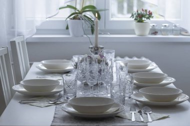 Gözlüklü bir yemek masası, tabaklar, yanan bir mum ve arka planda bir pencere..