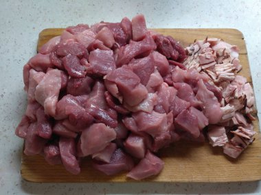 Çiğ domuz bacağı tahta bir tahtanın üzerinde küp şeklinde kesilmiş. Tahtada dilimlenmiş pastırma var. Malzemeler jambon üretimi için.