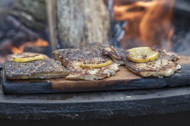 Taze balık ızgarada. Balığın üzerine bir limon tekeri konur. Yangın ortada görülebilir..