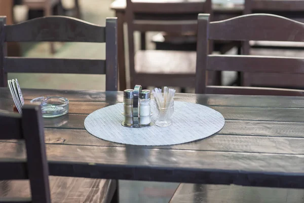 Brown table and chairs in the garden restaurant in sunny weather and on the table is salt shaker, pepper and ashtray