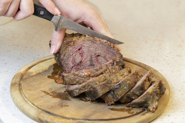 Hands of woman slices baked sirloin into slices.
