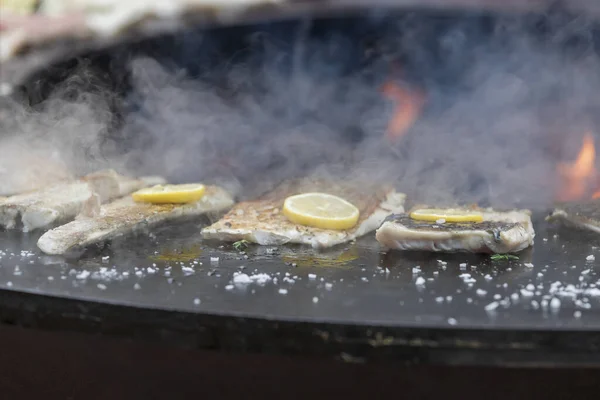 Fresh fish on the grill. A lemon wheel is placed on the fish. Fire can be seen in the middle.
