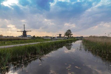Kinderdijk Holland 'da bir kanalın kıyısındaki yel değirmeni suya yansıyor. Arkaplan mavi gökyüzü.