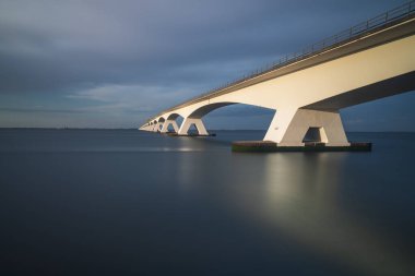 Hollanda 'da deniz üzerinden geçen güzel uzun Zeeland köprüsü. Gün batımında fotoğraf uzun zamandır. Gökyüzünde güzel mavi bulutlar var..