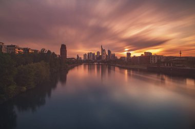 Gün batımında nehir manzaralı dramatik bir şehir.