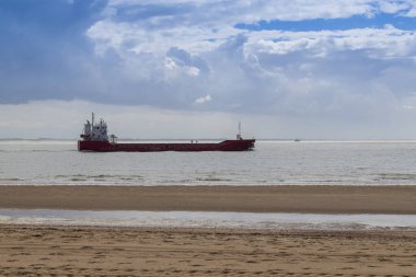 Hollanda 'nın Vlissingen kentindeki Kuzey Denizi' ndeki sahil ve kumlu plajlar. Arka planda fırtına bulutları ve denizde bir nakliye gemisi var..