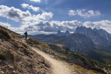 Yolda mavi ceketli bir kadın, İtalyan Dolomitleri 'nde. Güneşli havada ve mavi gökyüzünde bulutlar var..