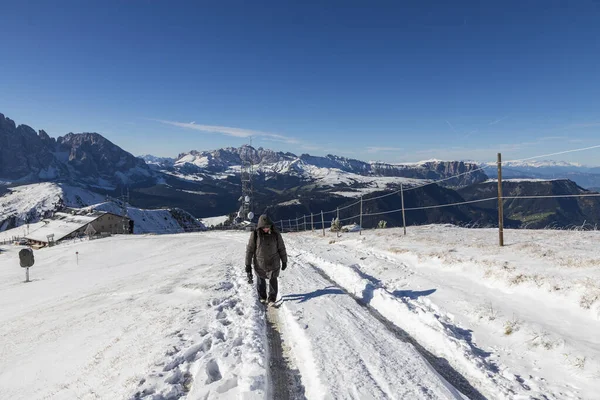 写真付きの暖かい冬のジャケットを着た女性は 晴れた日に雪の道を下り イタリアのドロミテのセセダ山の頂上に行きます 山の中は雪と雲に覆われた青空 — ストック写真