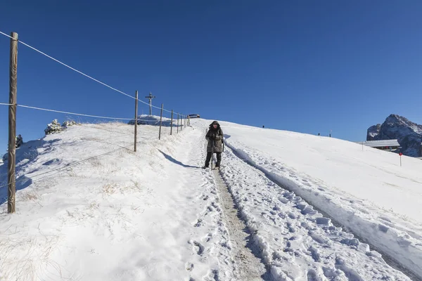 在晴朗的阳光灿烂的天气里 一位身穿保暖冬衣 头戴照相装备的女人沿着雪地的小径走到意大利白云石的塞西达山顶 山中有雪 蓝天有云 — 图库照片