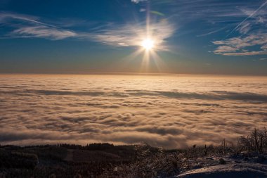 Sis ve bulutlarla kaplı harika bir kar manzarası. Batan güneş gökyüzünü boyuyor.