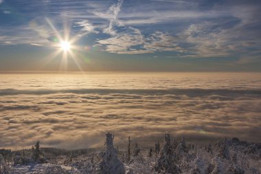 Sis ve bulutlarla kaplı harika bir kar manzarası. Batan güneş gökyüzünü boyuyor.