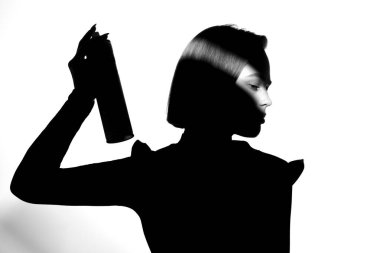 Black and white silhouette portrait with shadow and spot of light. The girl uses hairspray. Hair cosmetic concept.