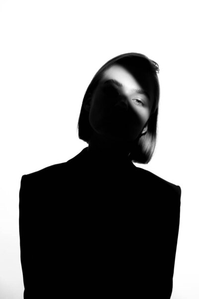 Fashionable beauty portrait. Black silhouette on white background. Girl with a spot of light on her face. 