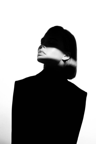 Fashionable beauty portrait. Black silhouette on white background. Girl with a spot of light on her face. 