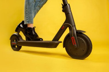 Elektrikli scooterlı güzel bir kız. Sarı arka planda izole edilmiş. Teknoloji ve hareket özgürlüğü.