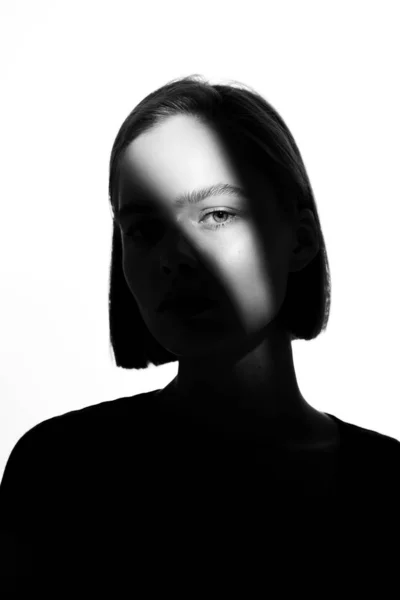 Moda bir güzellik portresi. Beyaz arka planda siyah siluet. Yüzünde ışık lekesi olan bir kız. 