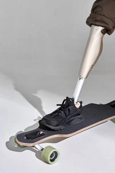 Инвалид молодой человек с протезом ног с длинным скейтбордом на белом фоне. Солнечный свет . — стоковое фото