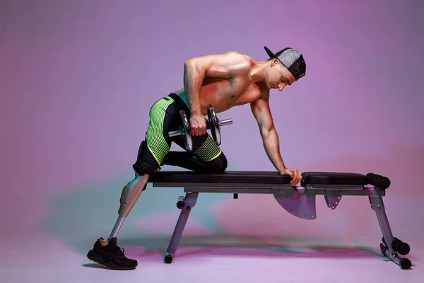 Um jovem homem musculoso com uma deficiência com uma perna protética está treinando em um ginásio com halteres. Cartaz de motivação . — Fotografia de Stock