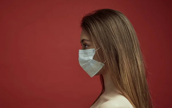 A young girl in a medical mask on a red background. Poster about the coronavirus COVID-19 pandemic. — Stock Photo, Image