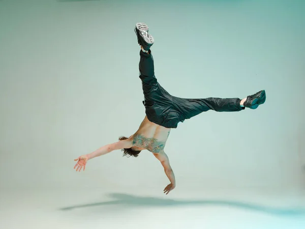 Un ragazzo giovane e aggraziato sta ballando una break dance sul pavimento senza maglietta. Trucchi complessi. Corpo con tatuaggi . — Foto Stock