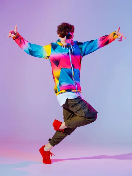 Guy dancing contemporary dance in studio. Neon light grey background. Acrobatic bboy dancer. Break dance lessons.