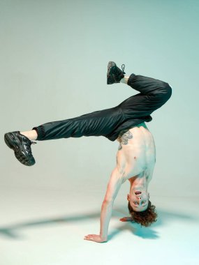 Genç ve zarif bir adam yerde tişörtsüz break dans yapıyor. Karmaşık numaralar. Dövmeli vücut..