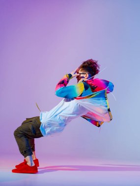 Stüdyoda çağdaş dans eden adam. Neon açık gri arka plan. Akrobatik bboy dansçısı. Break dans dersleri.