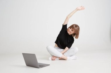 Havalı bir kız evde uzaktan jimnastik yapıyor. Dizüstü bilgisayarda uzaktan eğitim. Evde kalıp keyfine bak. 