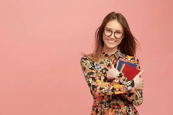 Genç, güzel bir kız öğrenci, elinde kitaplarla, tatlı tatlı gülümsüyor. Yabancı dillerin uzaklık öğrenimi.